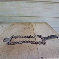 Vintage tire chain laid out flat on ground showing two parallel heavy chain links connected by solid metal ends and a strap clasping mechanism.