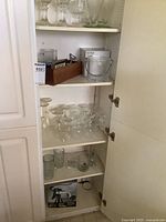 Shelf with various types of glass stemware including wine and sherry glasses, mugs, a small metal ice bucket and a wooden box with coasters and corkscrew on top