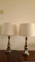 Pair of vintage brass table lamps standing side by side on a wooden surface, both with beige drum shades.