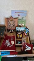 Display of wooden plaque, patches, pins, dogtag and flags all arranged in a box with Airborne Forces Museum flyer in background.