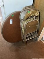 Vintage 36-inch round card table and 4 folding chairs leaning against wall in basement room