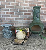 Wide shot of all items: chiminea, bird bath, frog fountain, solar lamp box against brick wall.