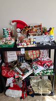 Wide view of multiple Christmas decorations displayed on shelving including textiles, ceramic tree pitcher, figurines, and assorted ornaments.