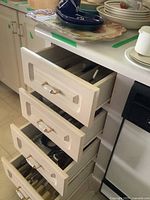 Four cream-colored drawers of kitchen cabinet shown with contents of kitchen utensils and cutlery organized inside.