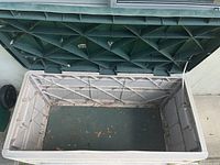 Open deck box showing interior with some leaves and dirt inside, textured green lid underside visible in background.