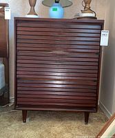 Front view of the Mid Century Modern 3-Drawer Dresser showing three horizontal slat drawer fronts, dark cherry finish, and tapered legs on beige carpet.