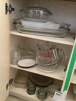 Glass covered casserole, pie plates, loaf pan, fruit nappies, measuring bowls inside cupboard, showing multiple glass bakeware items stacked and arranged.