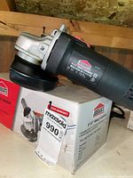 Angle grinder on top of its original box, showing the full tool and box brand and product image