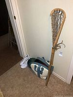 Vintage wooden lacrosse stick standing next to two bowling balls, a bowling bag, and a pair of white ladies shoes.