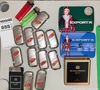Photo showing all items laid out: 11 silver Craven A lighters, 2 colored Tito lighters, 1 Benson & Hedges cartridge lighter, and 3 Macdonald Export A tins with branding graphics.