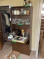 Full view of the wooden liquor cabinet / bookshelf with shelves holding various glassware and kitchen items, cabinet doors visible below.
