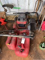 Photo of Briggs and Stratton lawn mower with grass catcher and two red plastic gas cans seen from above.