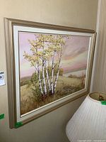 Framed oil painting of birch trees on a hillside with a pastel sky, hanging on a wall.