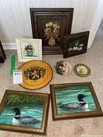 Photo displaying all items in the lot on carpet, including framed floral and loon paintings, two painted wooden plates, and floral coaster.