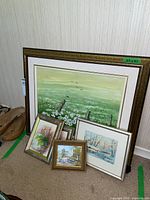 Group of five original framed paintings by Marya Dordowitz against wall on carpeted floor, including one large meadow landscape (25x21) and four smaller paintings.