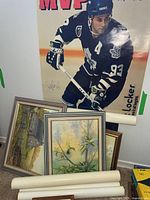 Four framed paintings stacked on the floor: two 12x15 landscape paintings and two smaller 5x7 paintings, in various frames, and rolled posters beside them