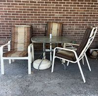 Four patio chairs with brown striped cushions and white metal frames arranged around a rectangular glass-top patio table with a white metal frame, with umbrella base visible underneath the table.