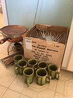 Photo showing cut glass punch bowl set boxed with cups and hooks, green ceramic mugs, and copper chafing dish with stand.