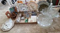 Photo of assorted serving dishes, plates, glass bowls, wooden geese figurines, and cutlery pieces placed on carpet.