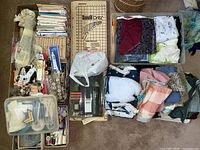 Wide view of sewing items including patterns, fabric, pincushions, tools, and basket on carpet floor showing lot contents