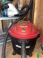 Red and black 5 gallon Shop Vac with hose and wheels, set on floor