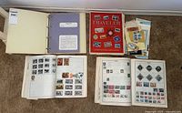 Four postage stamp albums laid out on the floor with stamps mounted in album pages and loose stamps and materials in translucent sleeves.
