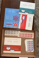 Box containing several souvenir cards from 1964 to 1967 and multiple small sheets of vintage Canadian postage stamps.