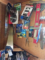 Photo of hand saws, saw blades, packaged drill bit sets, red level, and measuring tools on pegboard