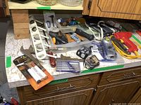 Overview photo of assorted hand tools and accessories laid out on countertop, including hammer, saws, plastic rack, electric stapler, screwdrivers, leveling tool, and touch-up paint markers.