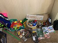 Overall view of assorted toys and art supplies including building blocks, die-cast cars, colored pencils, and small toys packed in boxes and containers.