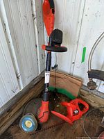 Black & Decker 18V electric hedge trimmer with battery, Grass Hog weed eater, and yard waste bags grouped together in a corner