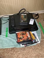 Photo showing the Citizen VHS player on top of the Toshiba DVD player with remote control and VHS cassette, along with a stack of DVD cases and VHS tape.