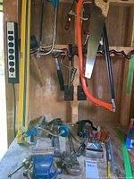 Worktable with mounted swirl base vise and assorted tools hanging on wall and on table.