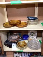 View of shelves showing amber glass ashtrays and other clear and colored ashtrays made of glass, porcelain, plastic, and stone.