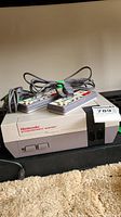 Front view of NES console with two wired controllers and power cords placed on top.