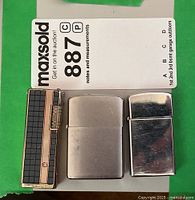 Three vintage lighters placed side by side: two Zippo lighters in silver finish and one Champ butane lighter with black grid pattern and copper trim.