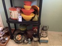 Wide view showing plastic storage containers stacked, vintage spinning canister set, cookie tin, coffee carafe, and blender on black shelving unit.