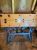 Full view of wooden top and metal base work mate table folded and placed against wooden wall.