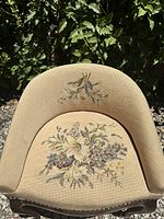 Top view of antique vanity stool barrel back showing hand-stitched floral needlepoint upholstery with flowers in cream, purple, and sage on a beige background with signs of light wear.