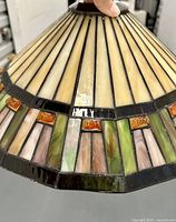 Close-up side angle showing the caramel vertical panels and colorful rectangular glass panels around the lower edge with leaded metal, showing texture and some wear on leading.