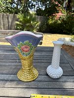 Two vases side by side on outdoor wood table with measuring tape showing sizes
