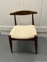 Front view of mid-century modern chair showing curved wooden backrest and cream upholstered seat.