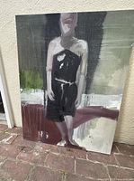 Photo of large-scale abstract figurative painting of a solitary figure in dark tones on canvas with expressive brushwork, shown leaning against a beige wall outdoors.