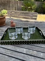 Green faux leather tray with brass-tone studs and four clear glass tumblers displayed on an outdoor wooden table.
