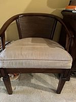 Front view of vintage barrel-style chair showing curved wooden frame, cane backrest, and upholstered neutral-colored seat cushion with some discoloration.