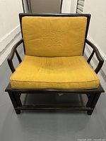Front view of ebonized wooden lounge chair with yellow silk cushion showing embroidered backrest pattern and wear on seat cushion.