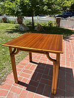 Square vintage table with wood top and bamboo-style rattan legs and frame in outdoor light.