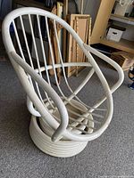 Side view of vintage white-painted rattan swivel chair showing curved armrest and vertical rattan rods forming the backrest and seat. Chair base also visible.