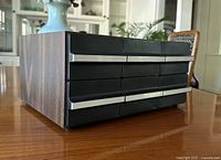Side-angle photo of the rectangular cassette tape organizer showing woodgrain sides and black drawers with silver handles