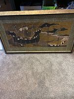 Full view of the framed artwork showing the large ship and smaller boat with figures in an Asian inspired design.